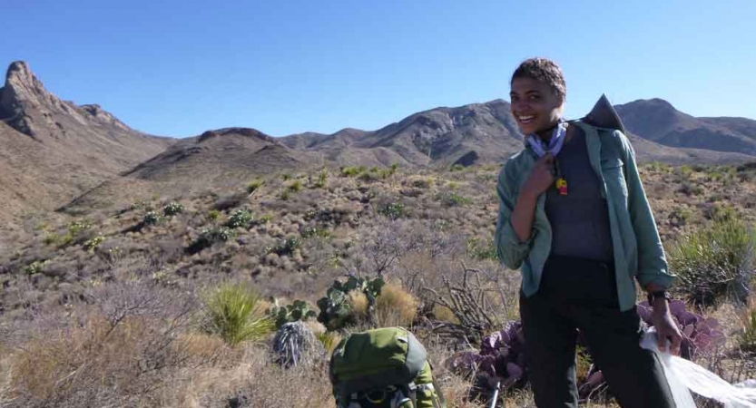 a student smiles at the camera in front of a desert landscape